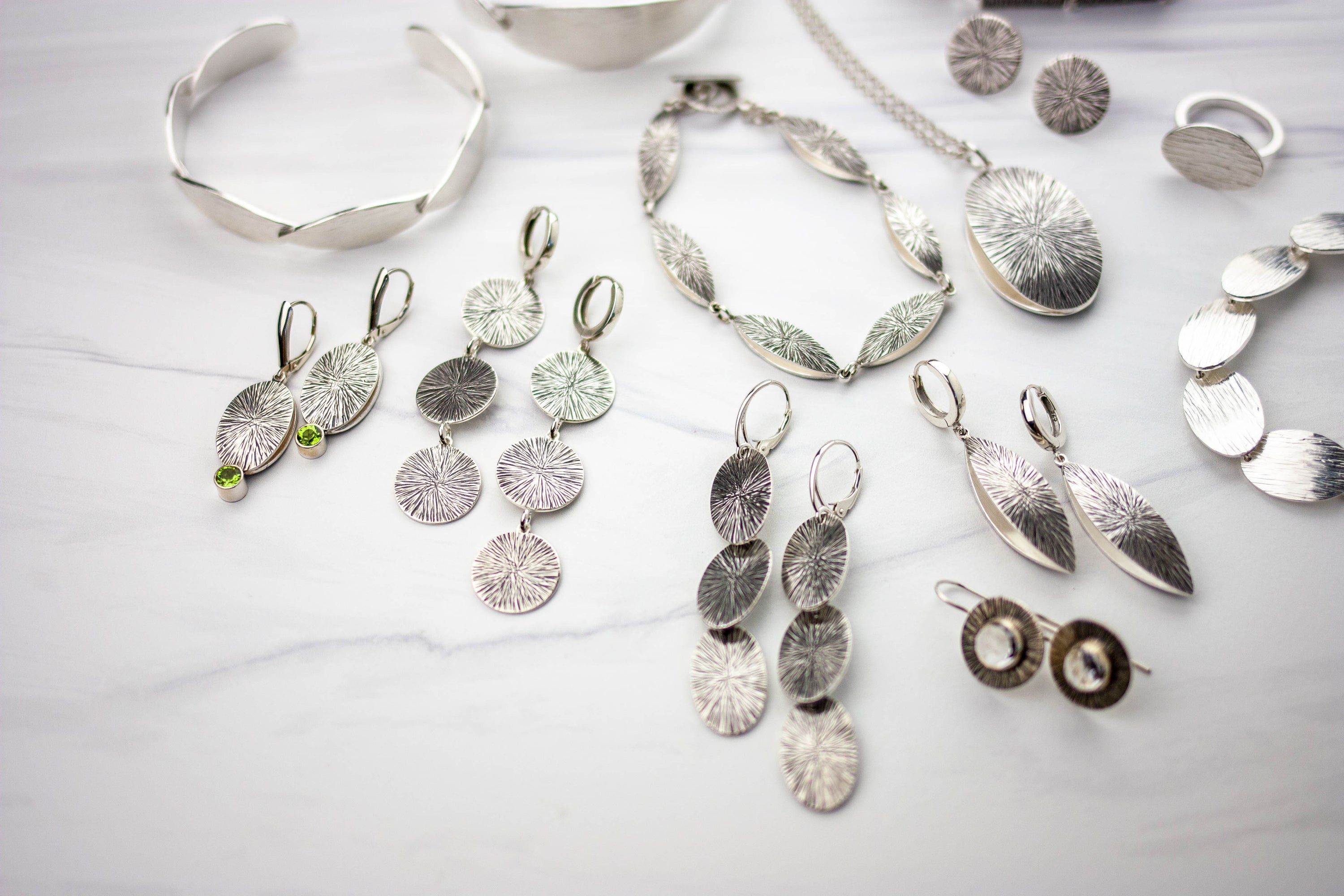 Collection of silver jewelry including necklaces, earrings, and bracelets on a light background. Houston, tx jewelry artist, geophilia studio.