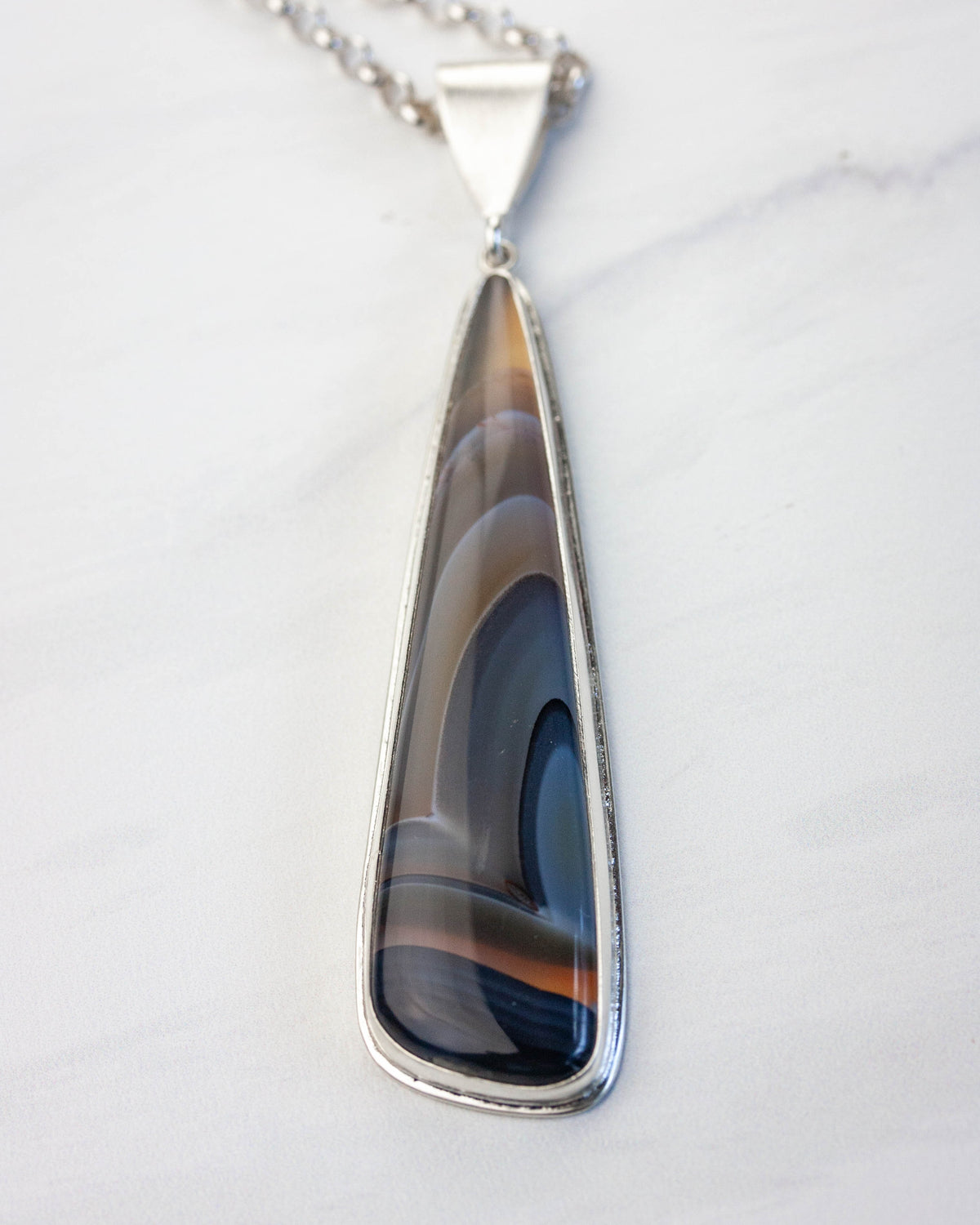 Teardrop-shaped pendant with a patterned stone on a silver chain against a white background
