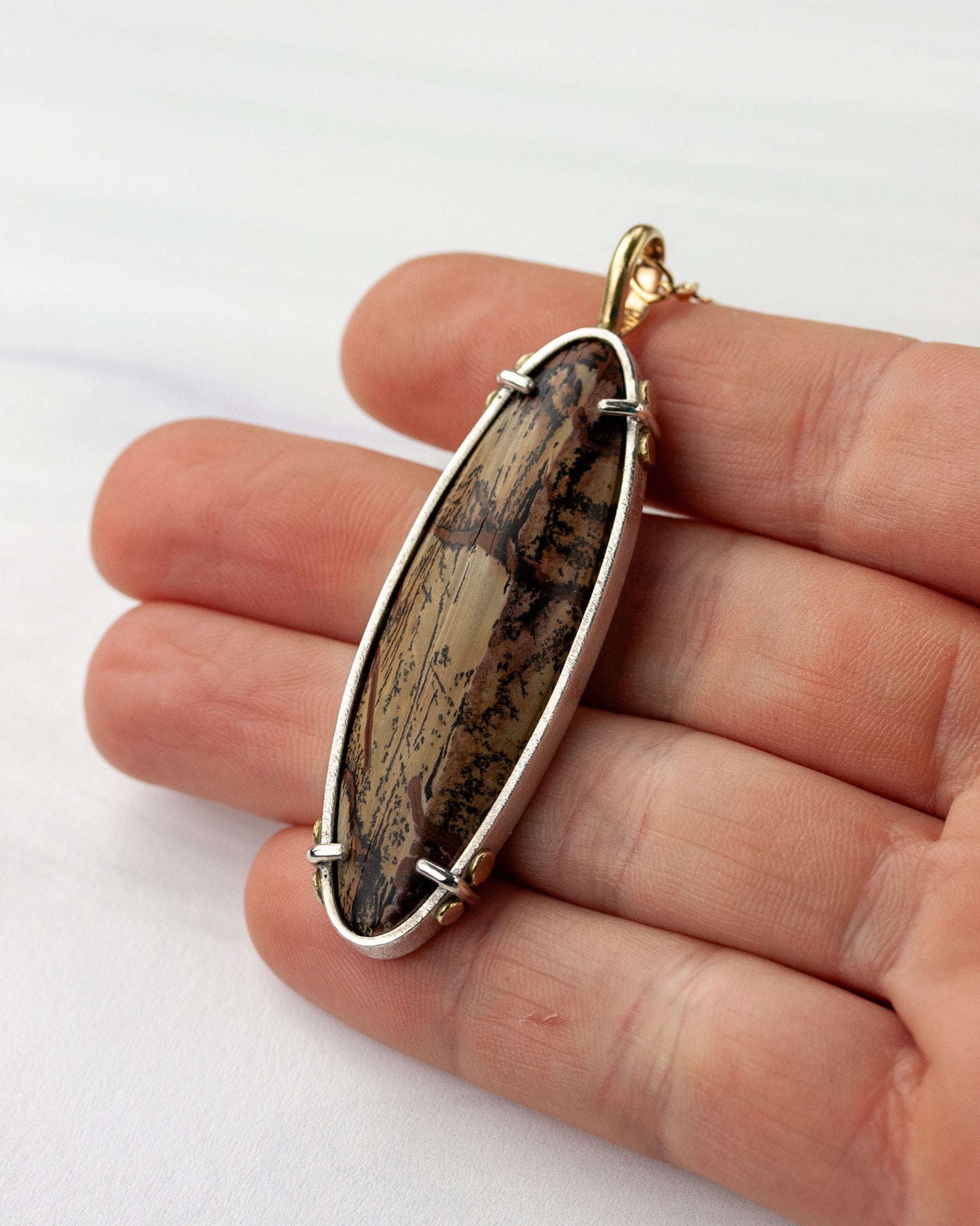 Hand holding Indian paint stone pendant in silver and gold for scale