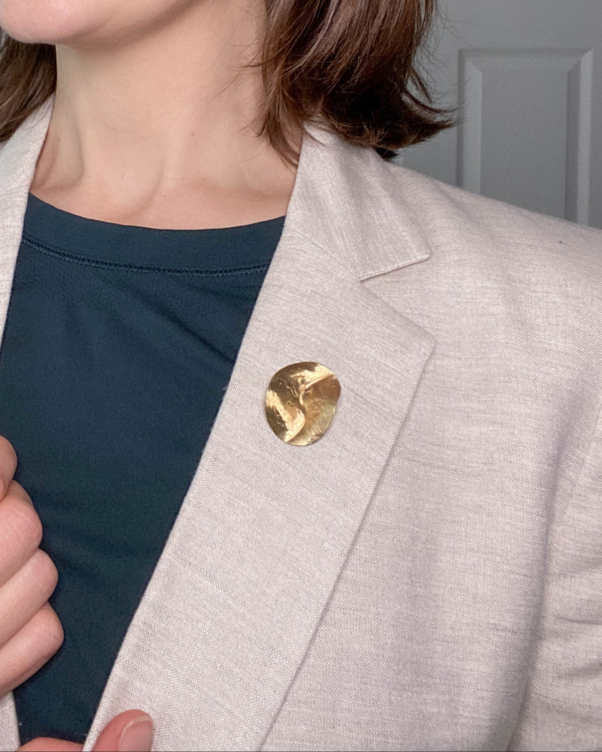 A brass brooch from the Contour Collection is pinned to a beige linen blazer. Brooch by houston, tx jewelry artist, Geophilia studio.