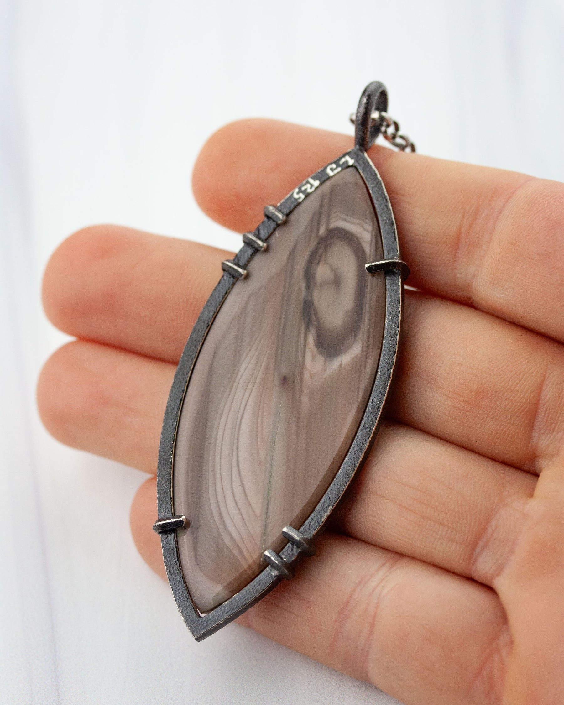 Hand holding Imperial jasper pendant in sterling silver for scale and showing artist signature on the back