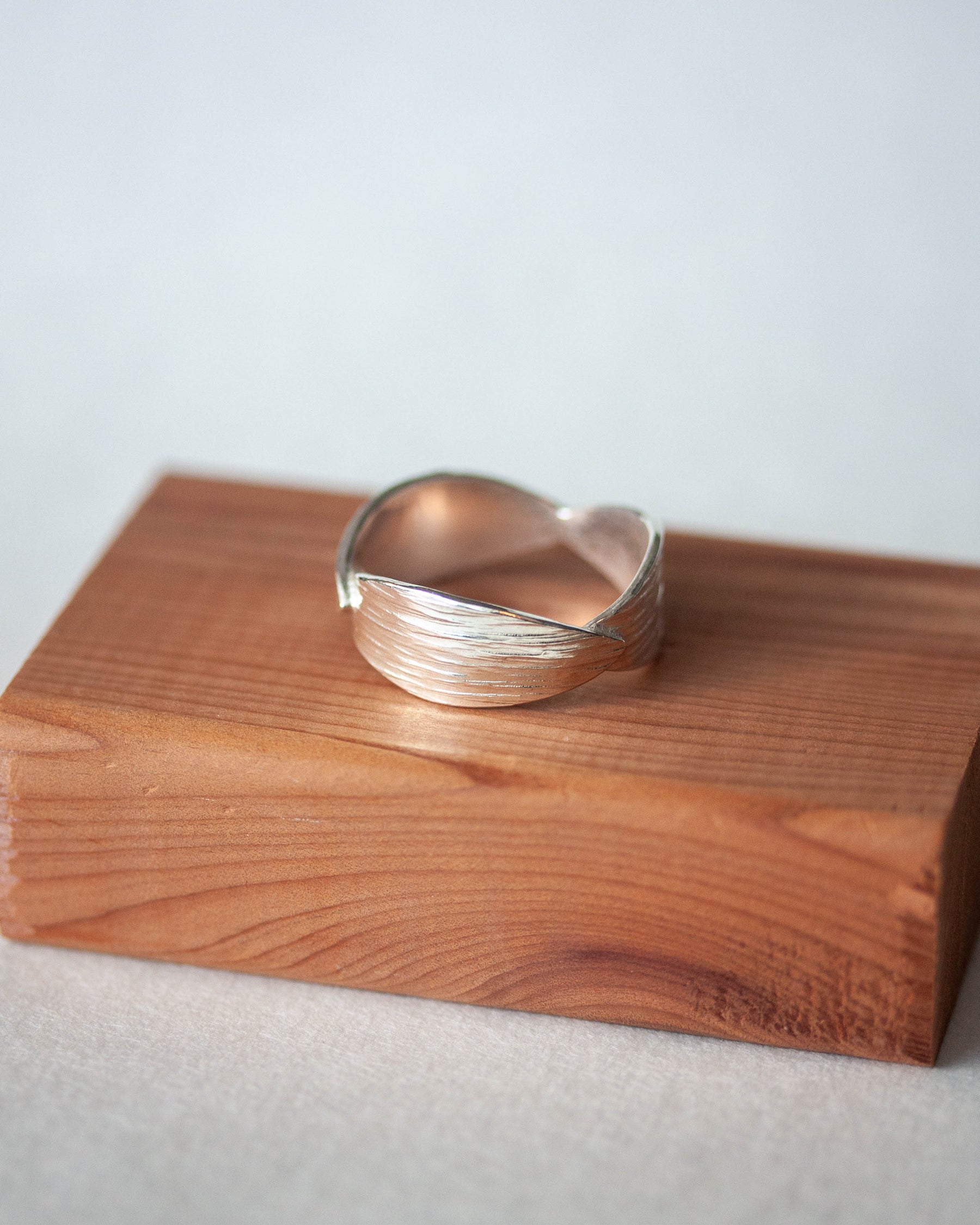 Silver ring on a wooden block with a light gray background