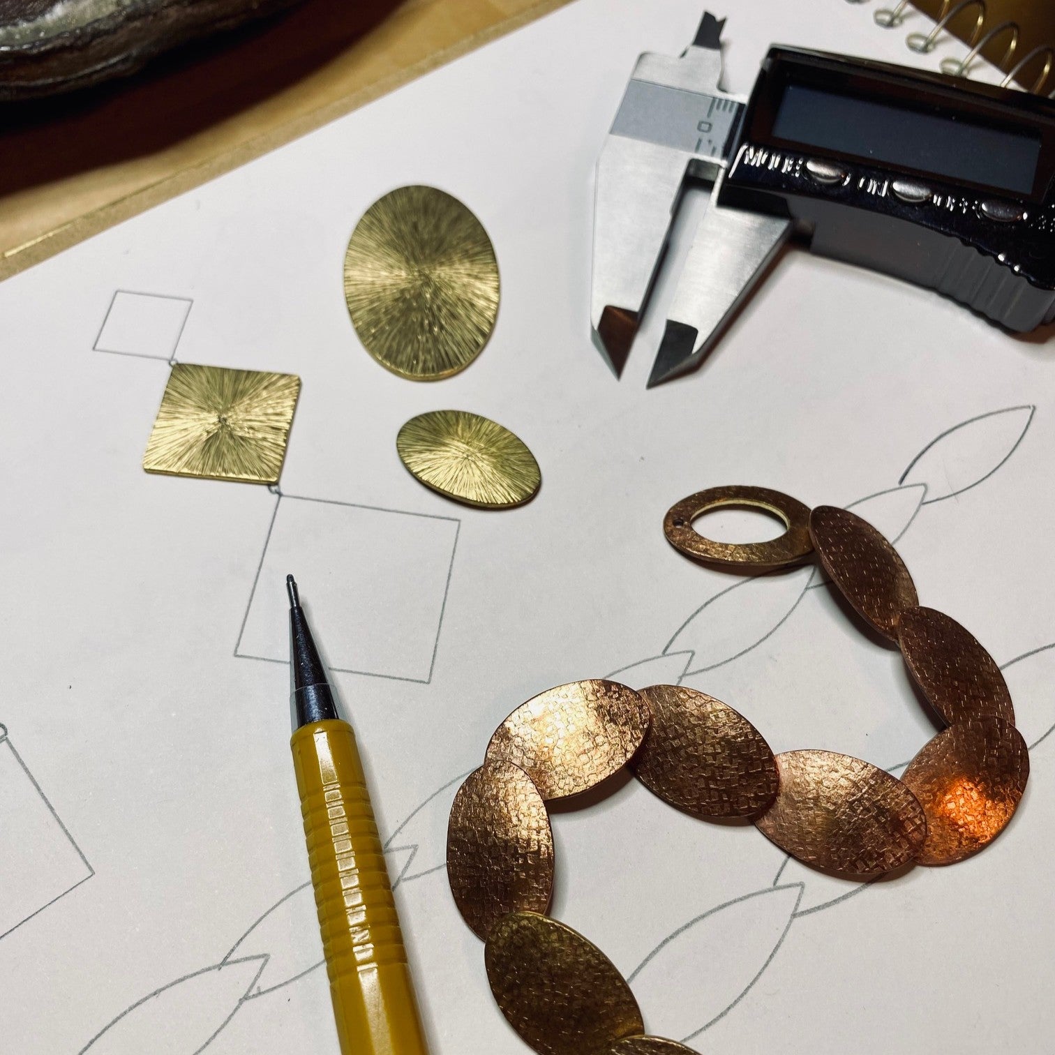 Unfinished jewelry components on a sketchpad with digital calipers and a pencil. 