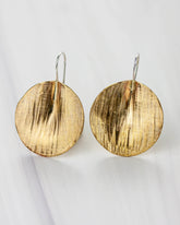 Golden bronze earrings on a white background. The shape is circular, lightly textured and folded to create a 3D effect.