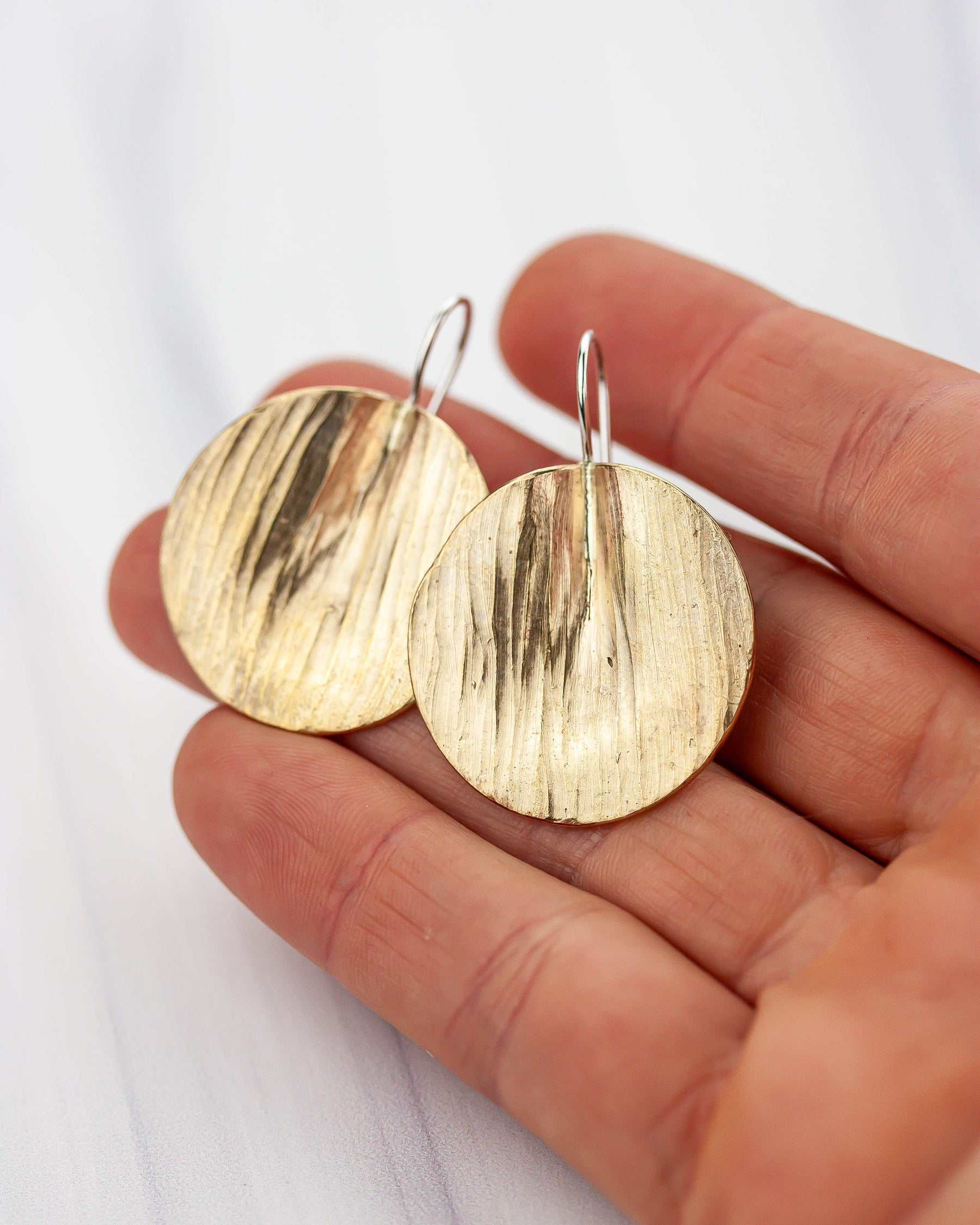 Golden bronze disc earrings held in a hand against a white background
