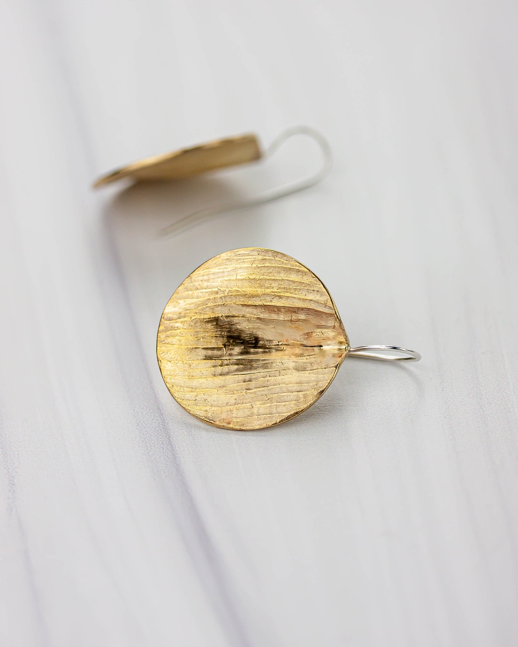 Golden bronze round earring on a white background. One is flipped over to show the silver ear wire.