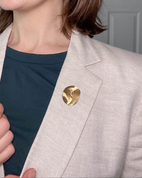 A brass brooch from the Contour Collection is pinned to a beige linen blazer. Brooch by houston, tx jewelry artist, Geophilia studio.