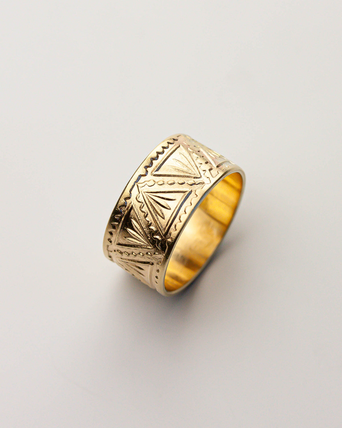 Golden brass ring with intricate patterns on a light gray background.