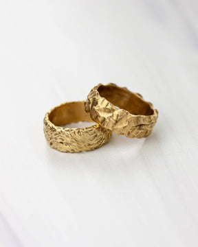 Two golden bronze rings each with a highly textured surface on a white background.