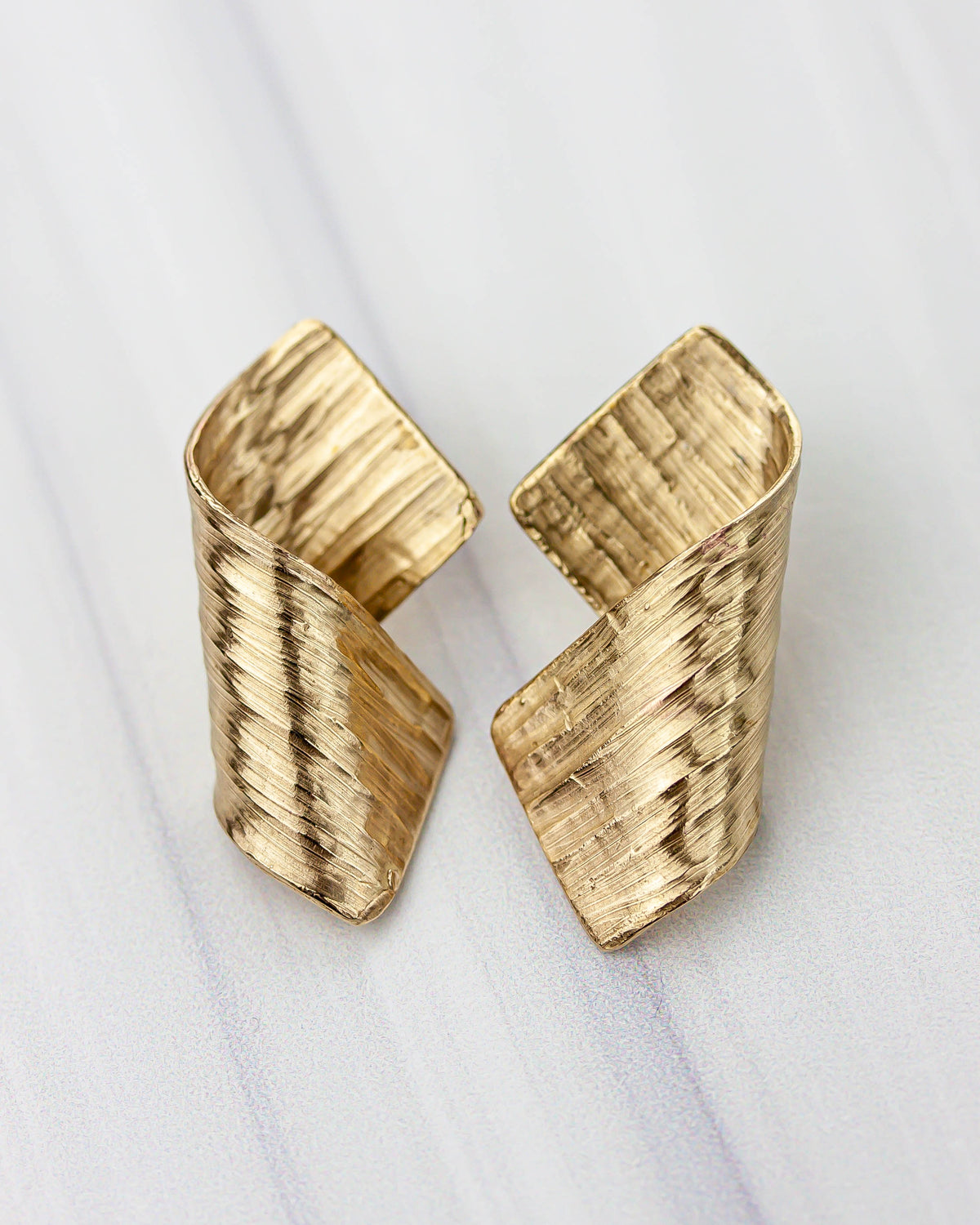 Golden bronze earrings on a white background. The shape is lightly textured and the metal is folded upon itself.