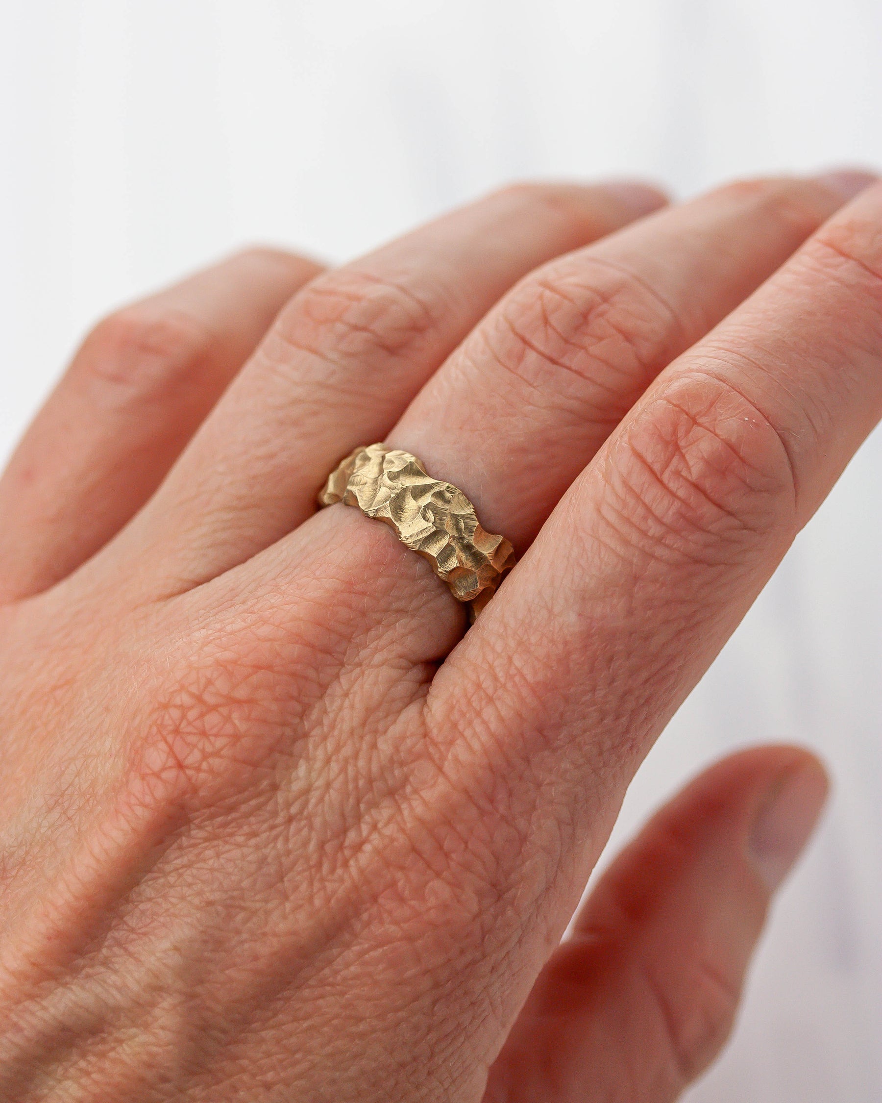 Golden bronze highly textured ring on a person's finger against a white background.