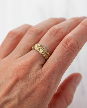 Golden bronze highly textured ring on a person's finger against a white background.