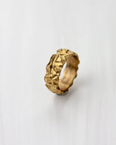 Golden bronze ring with a highly textured design on a light gray background.