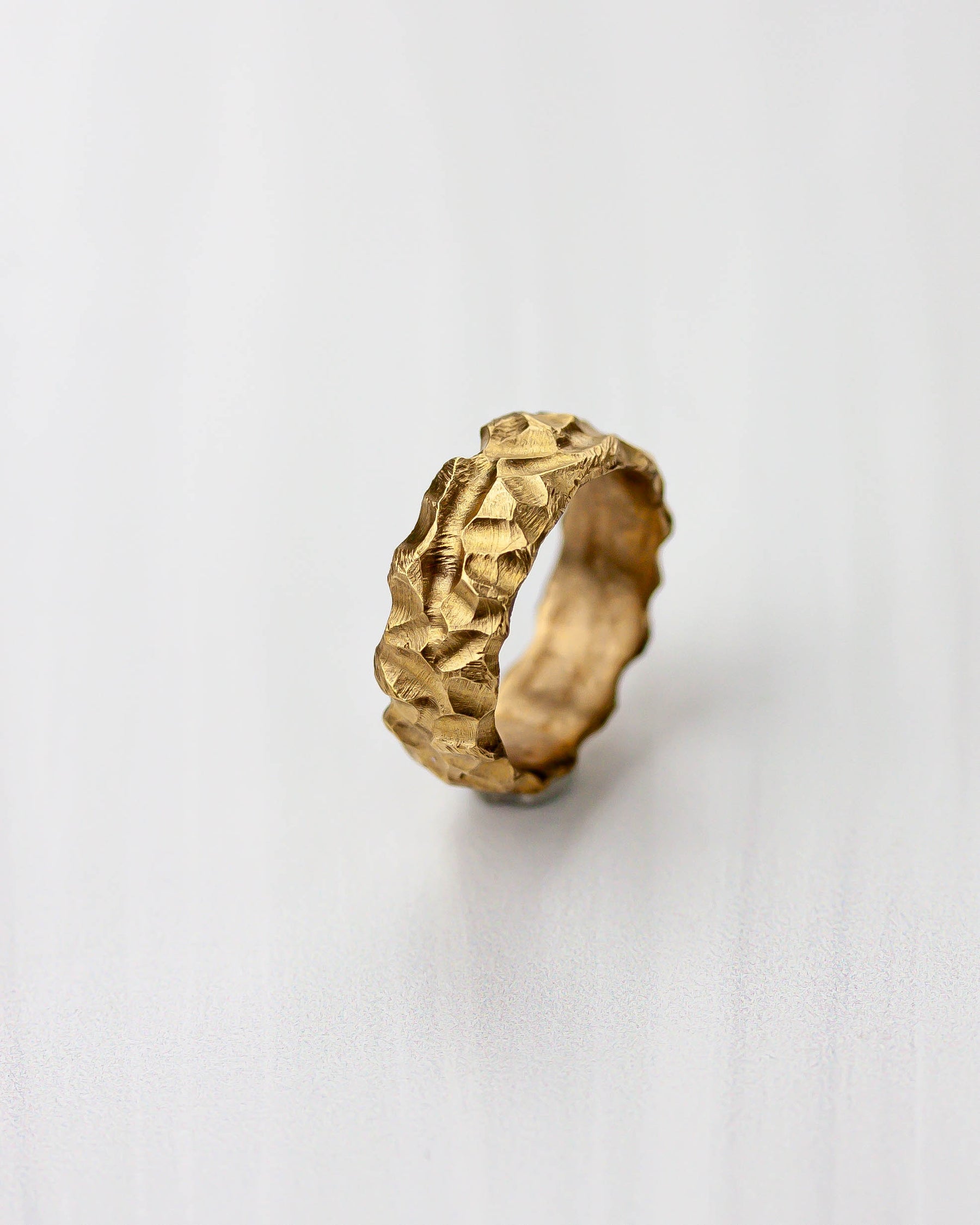 Golden bronze ring with a highly textured design on a light gray background.