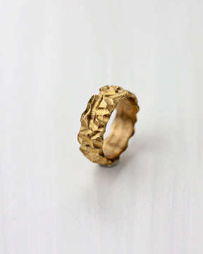 Golden bronze ring with a highly textured design on a light gray background.