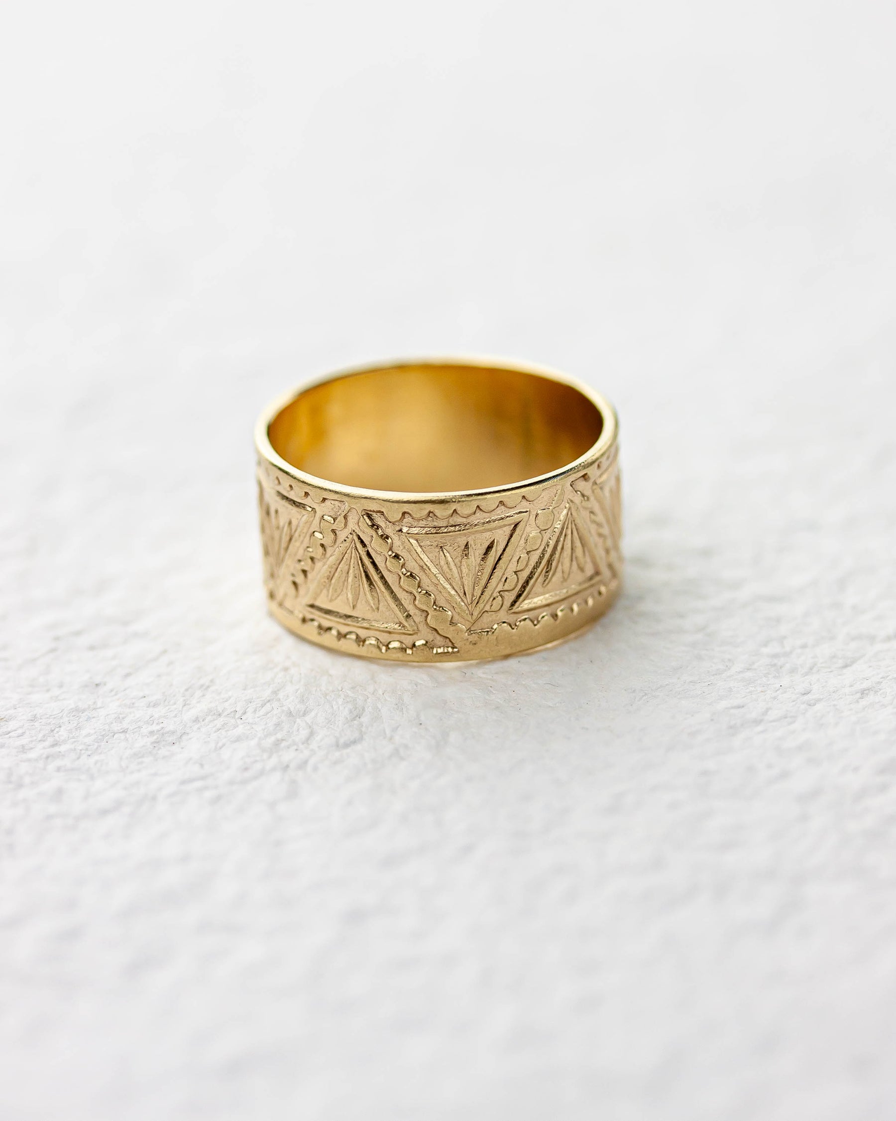 Golden brass wide band ring with geometric patterns on a white background.