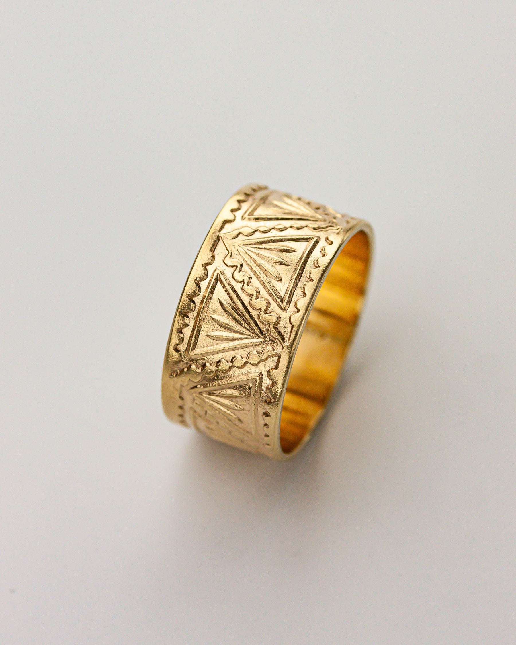 Golden brass ring with geometric patterns on a light gray background