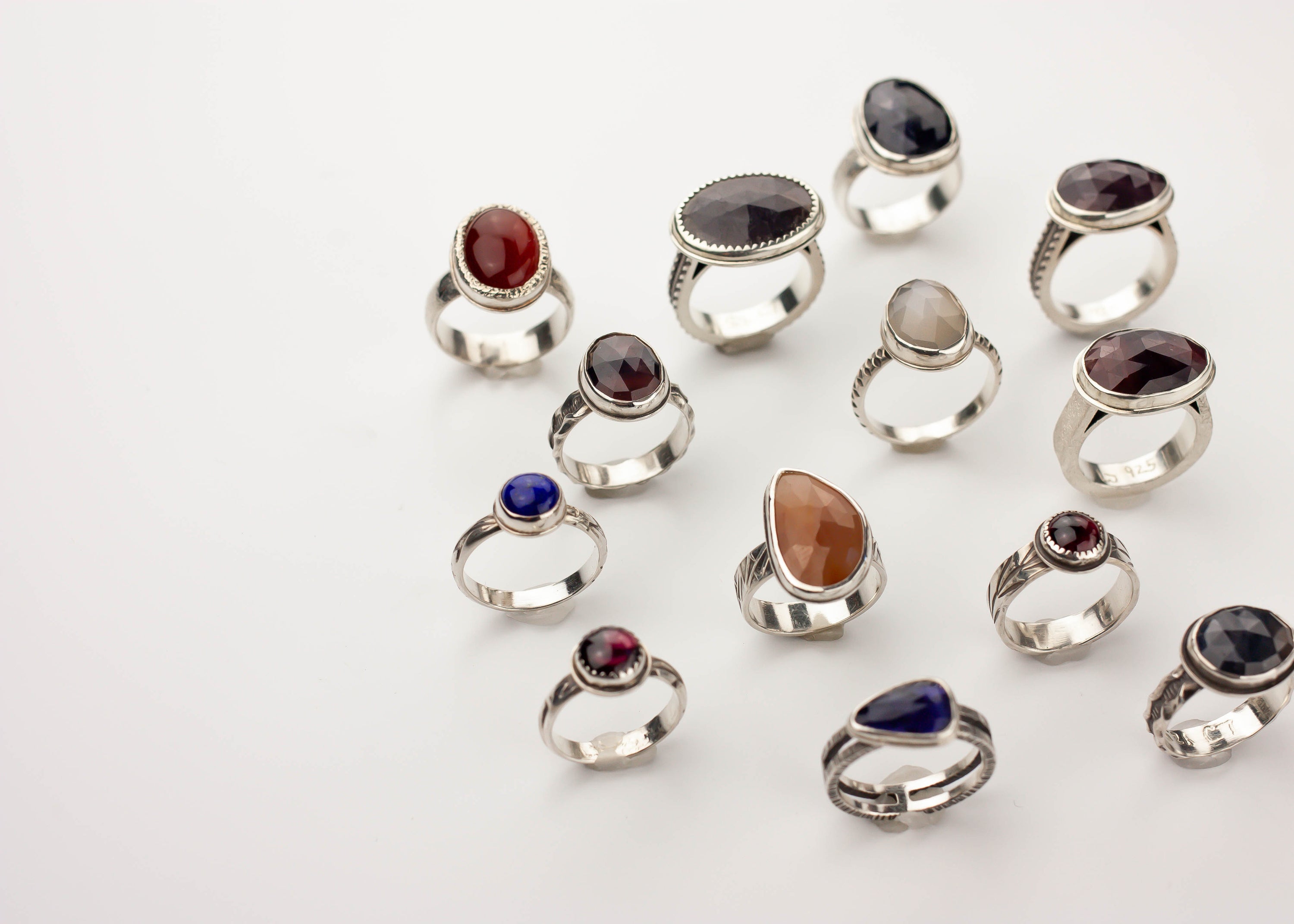 Collection of silver rings with various colored gemstones on a white background