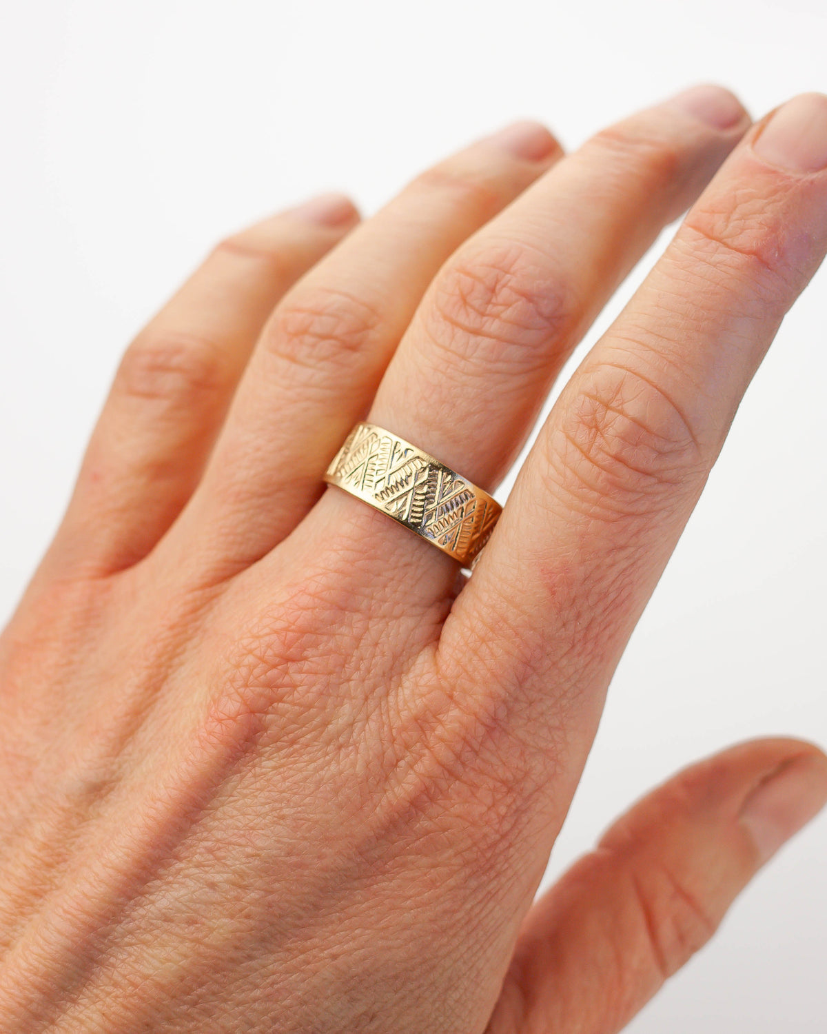 Golden brass ring with geometric pattern on a hand against a white background.