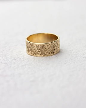Golden brass ring with geometric pattern on a light gray background