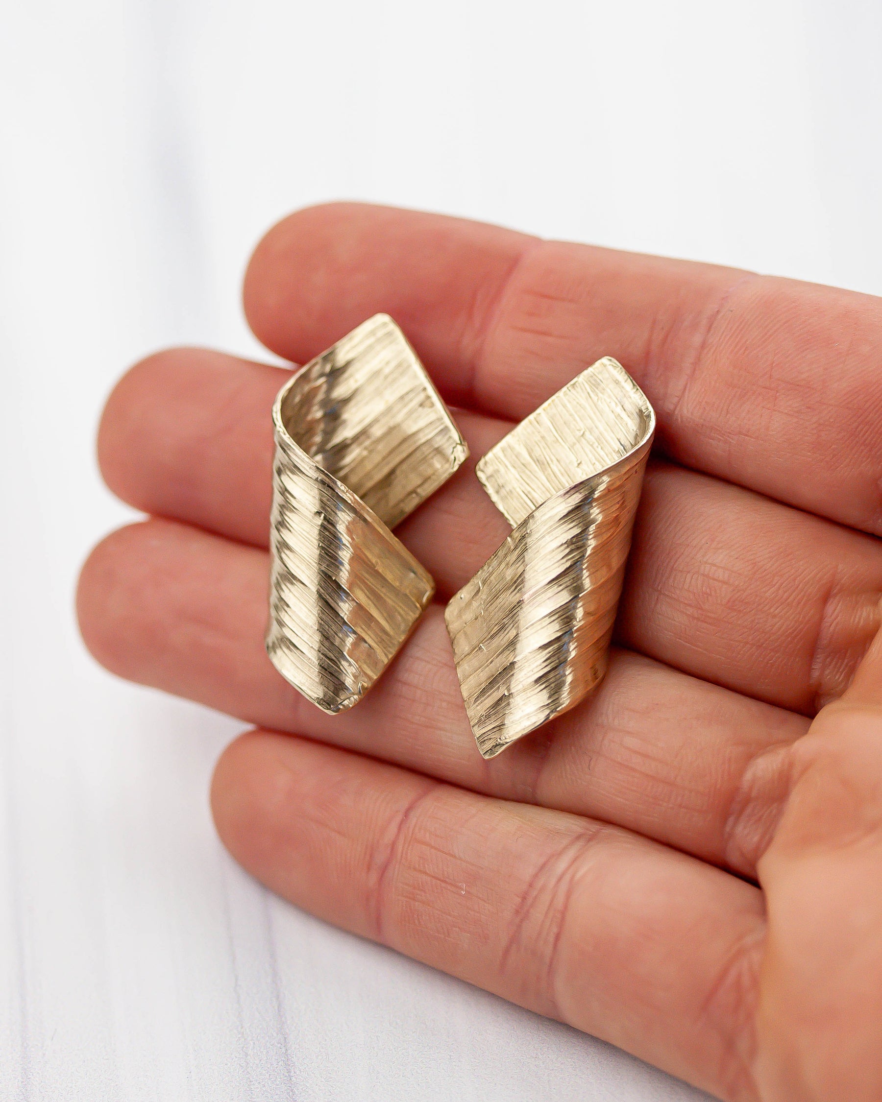 Golden bronze earrings held in hands with peachy skin. 