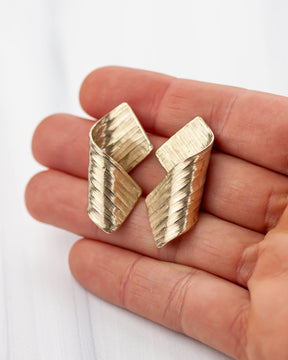 Golden bronze earrings held in hands with peachy skin. 